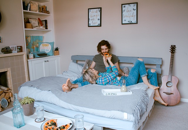 Žena a muž ležia v posteli a jedia pizzu
